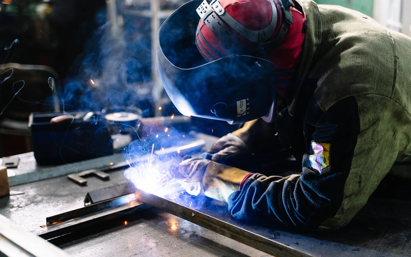 Industrial welder fabricating a steel frame assembly in a workshop